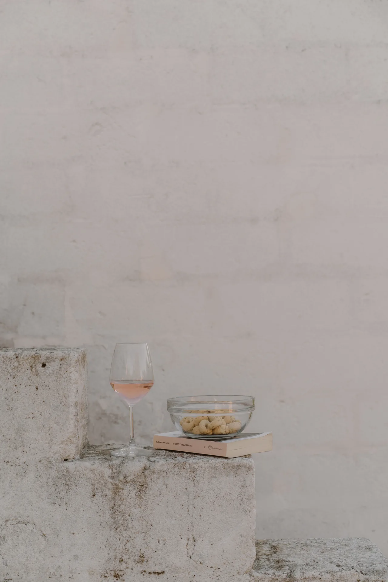 A glass of rosé and a bowl of almonds on the stone wall