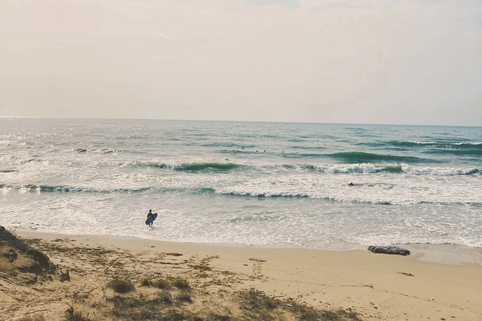 A surfer with a board on the beach at Campomarino, facing a rough sea