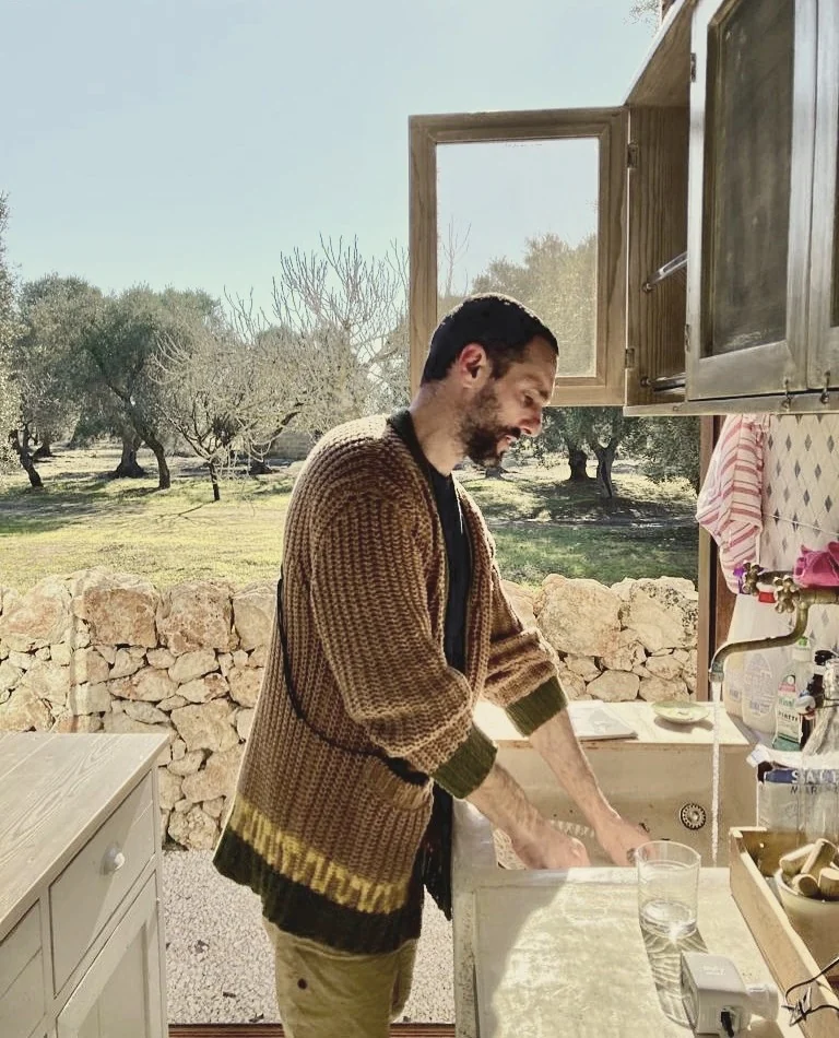 Valerio washing up in the kitchen open onto the olive grove, on 28 December, in a long cardigan