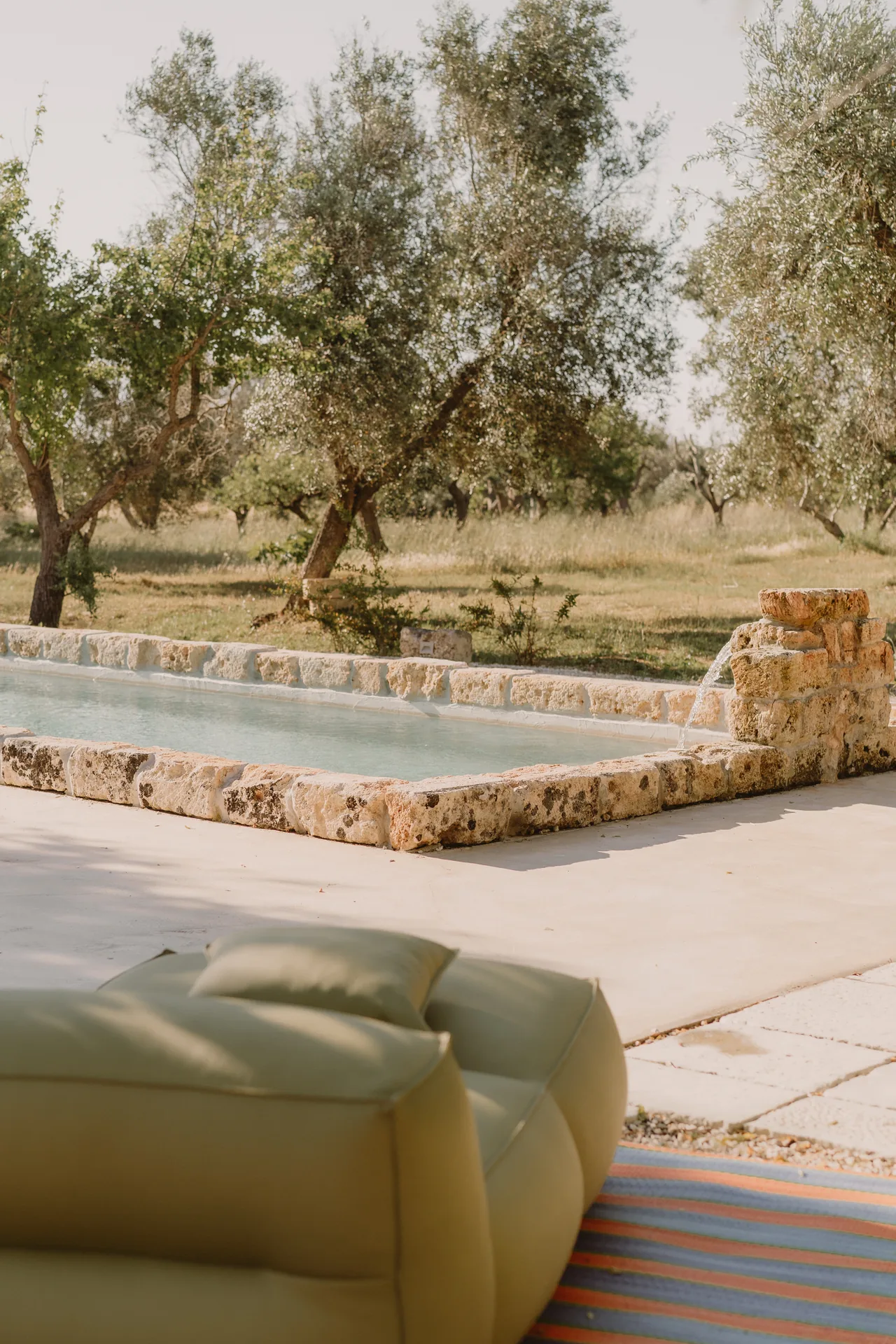 A yellow pouf by the pool, the olive grove beyond